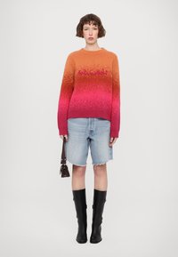 Sweter dzianinowy w gradientowych kolorach pomarańczowym do różowego, z prążkowanym dekoltem i tekstem. W połączeniu z jasnoniebieskimi szortami dżinsowymi i czarnymi botkami do kolan.