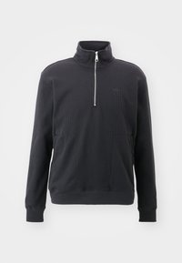 Sudadera negra con un alto cuello, cierre de mitad de cremallera en la parte delantera, textura acanalada y dos bolsillos frontales. Presenta un logo sutil en el pecho.