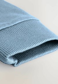 Himmelblaues, gestricktes Gewebe mit strukturiertem Rippenmuster am Bündchen, das eine glatte Oberfläche und einen gefalteten Rand aufweist. Keine sichtbaren Beschläge oder Muster.