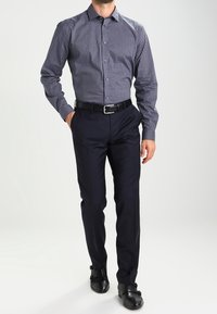 Kontrollerad, mörkblå skjorta med långa ärmar. Kombinerad med åtsittande mörka byxor och svarta skor, med en mjuk textur och subtil glans.