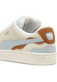 Puma suede sneakers met een crèmekleurige bovenkant, lichtblauwe accenten en een bruine suède hielafwerking. Geprofileerde witte rubberen zool.