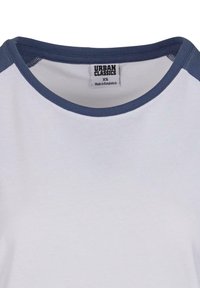 Hvid t-shirt med marineblå detalje ved halsudskæringen, der har en rund krave og mærker, der angiver brand og størrelse. Blødt bomuldsstof.