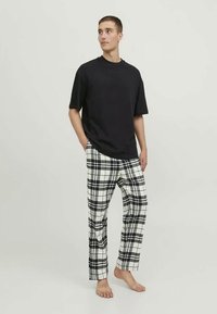 Musta lyhythihainen paita yhdistettynä valkoisiin ja mustiin ruudullisiin pyjamahousuihin. Housuissa on avara istuvuus, näkyvät taskut ja suorat lahkeet.