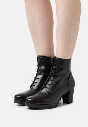 Botas de tobillo de cuero negro con cordones en la parte delantera, cremallera lateral, tacón grueso y textura suave. Apta para uso casual o formal.