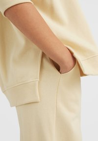 Felpa beige oversize con polsini a coste, tasca laterale e texture morbida, abbinata a pantaloni beige a vestibilità rilassata.