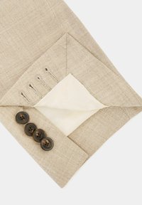 Manche de veste beige retournée montrant quatre boutons foncés et quatre boutonnières sur un tissu texturé avec une doublure intérieure blanche.