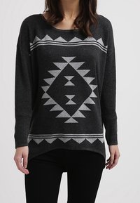 Pull gris avec un motif géométrique blanc, doté d'une coupe décontractée, d'un large décolleté et de manches longues. Fabriqué à partir d'un tissu doux et texturé.