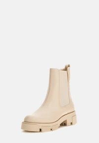 Beżowe botki za kostkę z gładkiej skóry, elastycznymi panelami bocznymi, teksturowanymi akcentami na obcasie oraz masywną podeszwą dla stabilności.