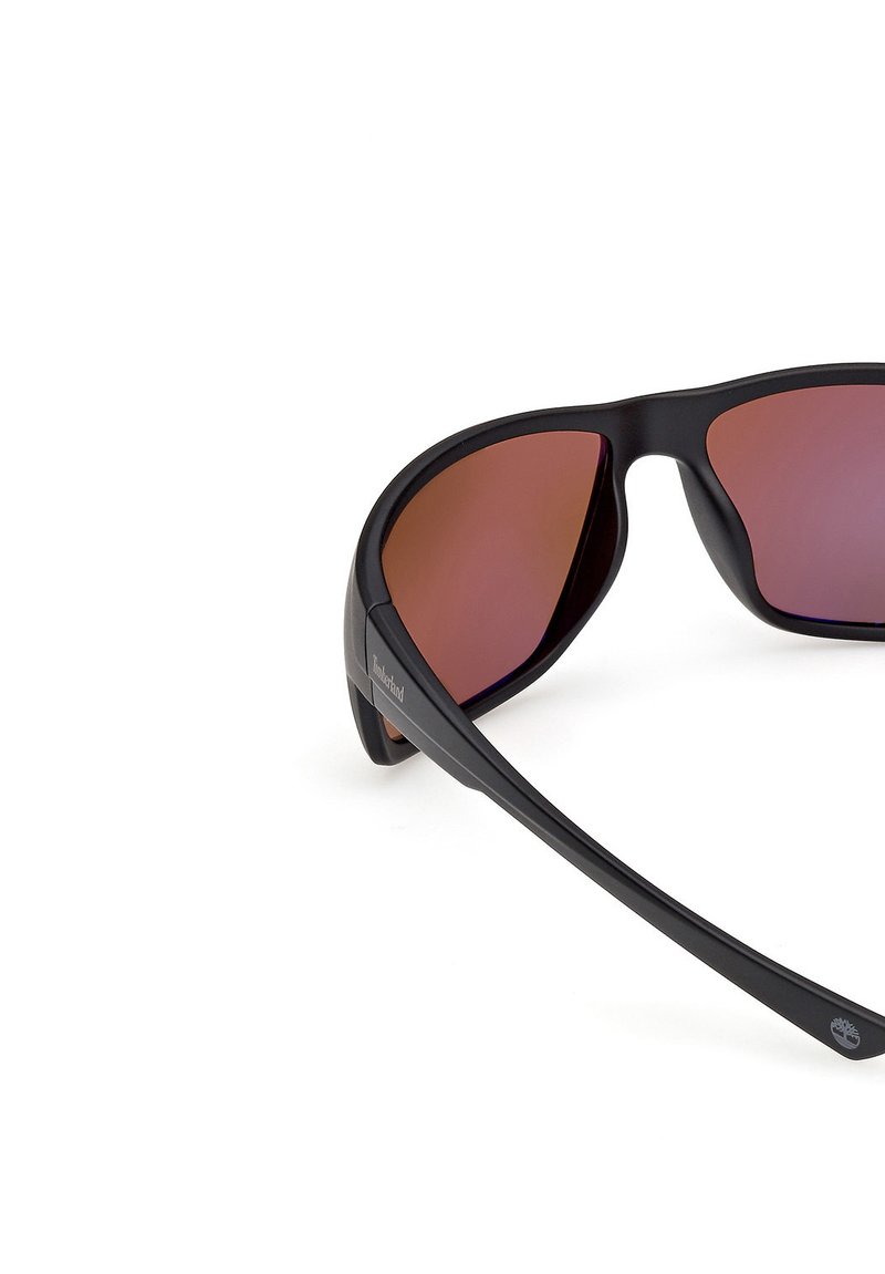 Lunettes de soleil noires avec un design enveloppant, dotées de verres teintés marron. Fabriquées dans un matériau léger avec une texture lisse et un accent de logo.