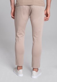 Beżowe spodnie slim-fit wykonane z lekkiego materiału, z nogawką węższą na dole i elastycznym pasem, w połączeniu z białymi sneakersami.
