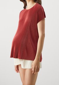 Top plisado rojo con mangas cortas y escote redondo, combinado con pantalones cortos de textura clara. Tejido suave, diseño fluido.