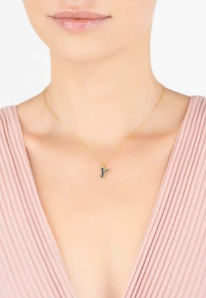 Gold chain necklace featuring a small black and gold letter "Y" pendant, worn against skin with a light pink top.