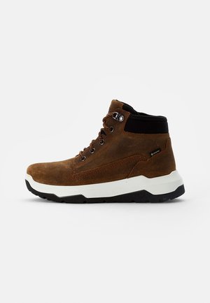 Braune Wildleder-Wanderschuhe mit einem schwarzen gepolsterten Kragen, weißer Zwischensohle und strukturiertem Gummi-Außensohle. Mit metallischen Ösen und braunen Schnürsenkeln.