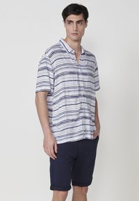 Krátky rukáv, zapínanie na gombíky, biela košeľa s horizontálnymi námorníckymi modrými pruhmi, s voľným strihom a golierom.