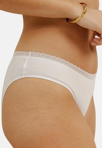 Sous-vêtements en coton blanc avec une bordure en dentelle festonnée à la taille, présentant une texture lisse et un design simple.