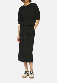 Ensemble noir en deux pièces comprenant un haut ample à manches courtes et une jupe mi-longue avec poches. Assorti à des baskets beiges.