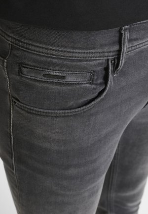 Jeans de denim gris oscuro con un diseño clásico, que presentan un bolsillo trasero con una chapa rectangular y detalles de costura sutiles.