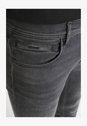 Jeans de denim gris oscuro con un diseño clásico, que presentan un bolsillo trasero con una chapa rectangular y detalles de costura sutiles.