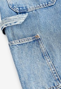 Tissu denim bleu clair en gros plan montrant une couture pliée et une poche arrière rectangulaire avec des coutures orange.