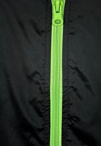 Fermoar verde strălucitor închis pe material negru, arătând clar cârligul și dinții fermoarului.