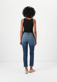 Zwarte geribbelde tanktop, blauwe denim jeans met contrasterende stiksels. Platte tan kleurige schoenen met een klein knoopdetail en een gecropt enkelmodel.