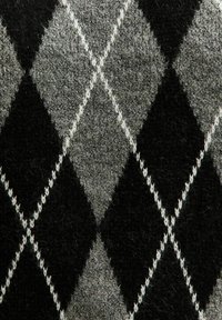 Primer plano de una tela de lana con un patrón de diamantes argyle en negro y gris, bordeado por líneas blancas cosidas.