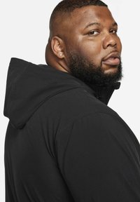 Zwarte hoodie met ritssluiting en trekkoord in de capuchon, textuurstof en een nauwsluitend ontwerp. Opvallende details zijn een soepele ritssluiting en gestikte naden.