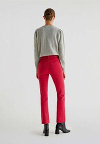 Grå strikket sweater med puffede skuldre, parret med røde tætsiddende jeans og sorte ankelstøvler. Outfittet har et rent, moderne design.