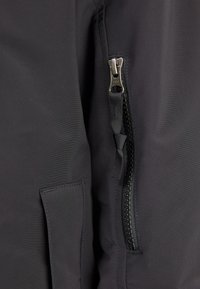 Giacca isolante nera con tasca laterale e una zip robusta. Tessuto morbido e design elegante evidenziato da cuciture a contrasto.