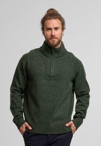 Donkergroene fleecetop met een hoge kraag, kwart-rits aan de voorkant en geribbelde manchetten en zoom. Zachte textuur met een ontspannen pasvorm.