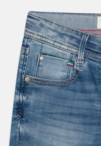 Džínové kalhoty v světle modré barvě s odřením, pěti-kapsový design, mosazné komponenty a kontrastní šití. Logo štítek v zelené, bílé a červené barvě.