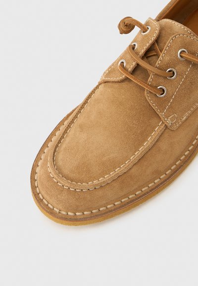 Παπούτσι από μοσχάρι σουέντ σε καφέ απ όχρωση, με στρογγυλή μύτη, δερμάτινα κορδόνια, μεταλλικά κρικάκια, αντίθετη ραφή, λεία υφή, ελαφρύ τακούνι και ανθεκτική λαστιχένια σόλα.