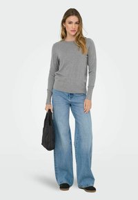 Grijs lange mouwen sweater met ronde halslijn en knoopdetails op de manchetten, gecombineerd met wijde blauwe jeans en een zwarte tas.