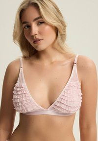 Jasnoróżowy biustonosz braletka z falbaniastym wykończeniem przy miseczkach, z cienkimi regulowanymi ramiączkami i bezszwowym pasem. Miękka tekstura.