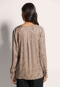 Beige Langarmhemd mit einem dezenten Camouflage-Muster, glatter Textur, rundem Ausschnitt und seitlichem Falten-Detail.