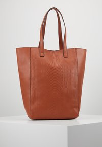 Bruine leren schoudertas met textuur aan de zijkanten en een gladde bovenkant. Dubbele handvatten en ruim ontwerp zonder zichtbare hardware of accenten.