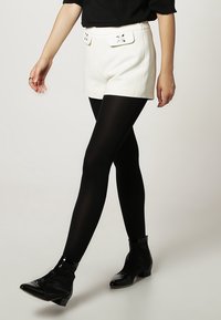 Vita högmidjade shorts med struktur och dekorativa fickor, kombinerat med svarta strumpbyxor och glänsande ankelskor.