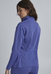 Lila, langärmliges Oberteil mit hohem Kragen aus strukturiertem Stoff, figurnaher Silhouette, gerippten Details an den Bündchen und dem Saum.