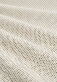 Primo piano di un tessuto a maglia a coste color crema con texture visibile e morbide pieghe che creano onde delicate.