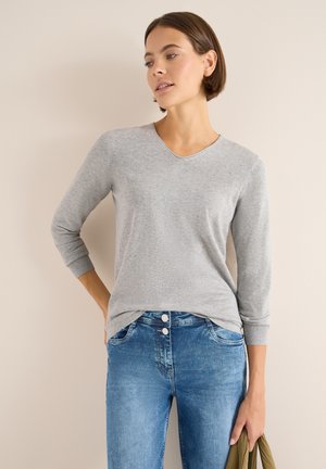 Graues Langarmoberteil mit V-Ausschnitt, aus weichem Stoff, kombiniert mit hellblauen Jeans mit Knopfverschluss und Seitentaschen.