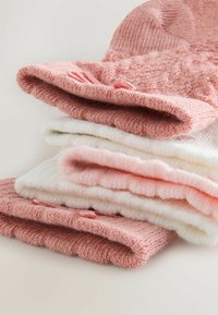 Rinkinys sulankstytų kojinių rožinės ir baltos spalvų atspalvių. Yra tekstūruotų raštų, minkštos megztos medžiagos ir švelnūs storio skirtumai.