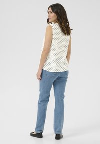 Blouse sans manches blanche à pois noirs, associée à un jean bleu clair et des ballerines noires. Tissu lisse, coupe décontractée, ourlet arrondi.