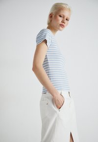 Lyseblåstripete kortermet topp laget av ribbet stoff, kombinert med et hvitt denimskjørt med en frontsplitt og detaljer med baklomme.