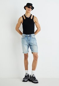 Débardeur noir sans manches avec des bretelles découpées, short en denim bleu clair retroussé à l'ourlet, chapeau seau noir et baskets de sport grises.