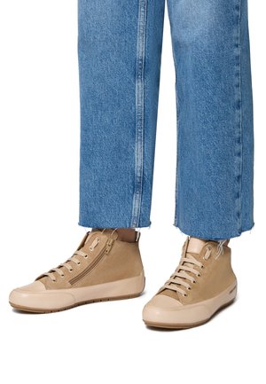 Beżowe sneakersy typu high-top z kombinacją skóry i zamszu, z zapięciem na sznurówki i zamek błyskawiczny, na tle niebieskich spodni dzwonowych.