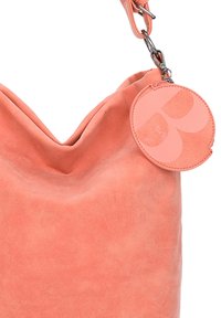 Sac à bandoulière en daim rose corail avec une étiquette ronde assortie attachée au fermoir en métal de la sangle.