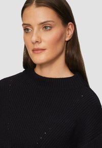 Dunkelblauer, gerippter Pullover mit hohem Kragen und dezenten Texturdetails, der vertikale Rillen und kleine Aussparungen aufweist.