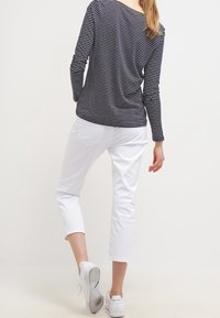 Granatowo-biała koszulka w paski z długim rękawem, zestawiona z białymi spodniami o długości do kostek i białymi trampkami, widziana od tyłu. Gładka faktura tkaniny.