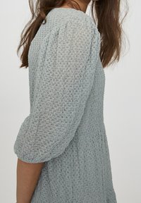 Vestido azul claro texturizado con mangas abullonadas y un escote redondo, que presenta un tejido estampado y una silueta acampanada.