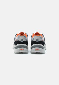 Baskets noires et grises avec un design texturé, accents orange, col rembourré et semelle blanche avec un motif tacheté et détail de logo.